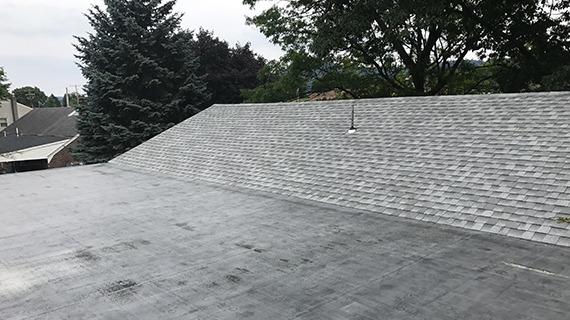 Finished roof with dark shingles on a slanted part and black waterproof coating on flat area