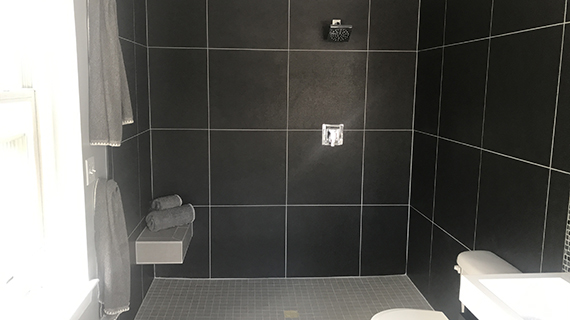 bathroom shower with large black tile walls and small grey tile floor