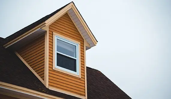 picture looking up at a dormer window with mustard yellow siding