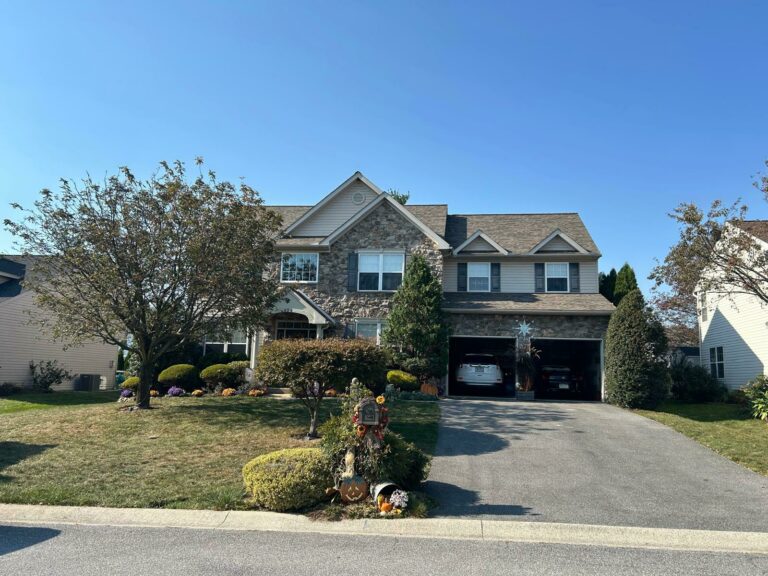 A stone house with a driveway, a spacious front yard with a tree and some decorations, tan siding, a two-car garage, and a New Owen's Corning Roof in Blandon PA